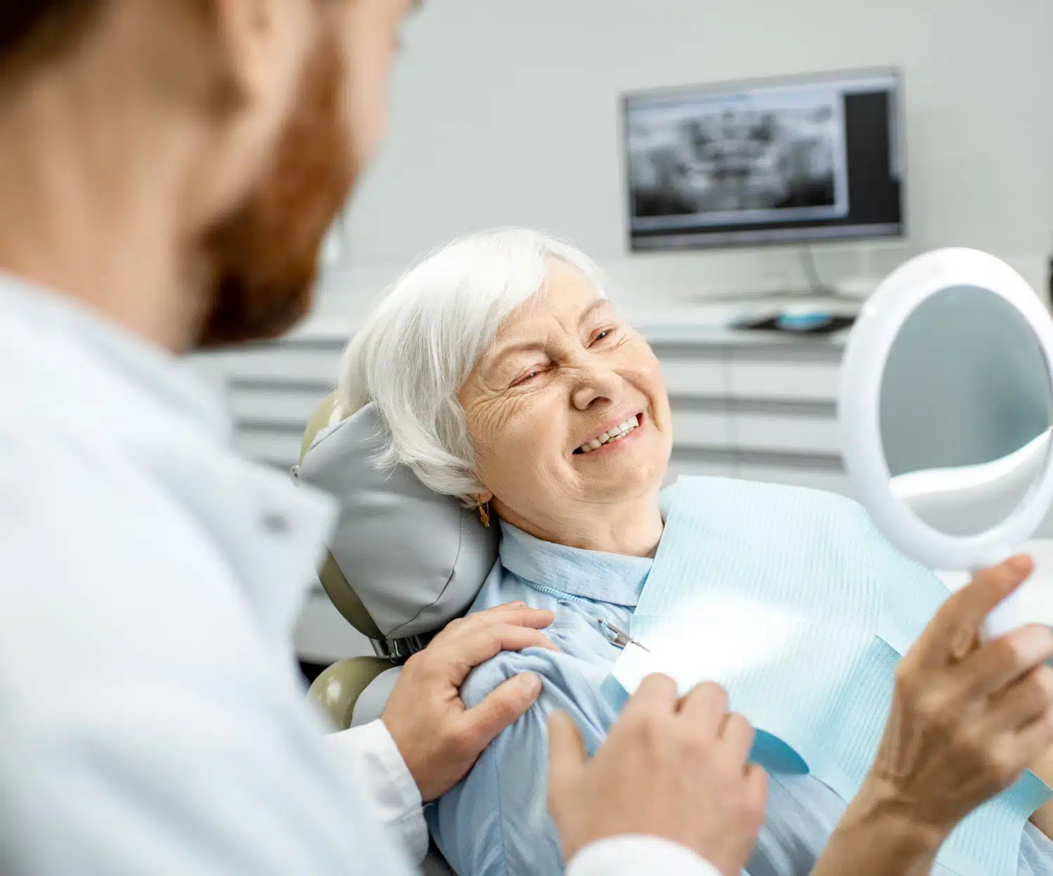 Older patient looking happy at the mirror sitting in the dentist chair